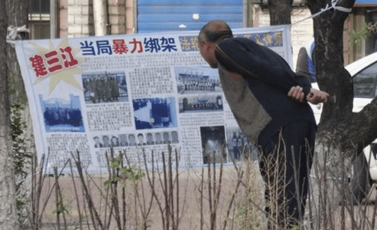 A Chinese citizen in Jiamusi, Heilongjiang Province, reads a banner hung by Falun Gong practitioners in 2018 that reads “Kidnapped by Authorities” detailing persecution cases in the area (Credit: Minghui.org)